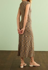 Maxi-Strickkleid in Braun, Beige und Blau mit kurzen Ärmeln, strukturiertem Muster und taillierter Silhouette. Kombiniert mit Riemchensandalen.