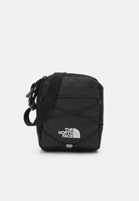 Borsa a tracolla nera con superficie testurizzata, caratterizzata da un logo bianco, tracolla regolabile e dettaglio elastico incrociato sulla parte frontale.