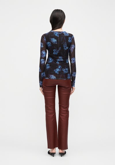 Langärmeliges Hemd aus schwarzem, transparentem Stoff mit blauem Blumenmuster, kombiniert mit burgunderroten Lederhosen. Das Outfit hat eine taillierte Silhouette.