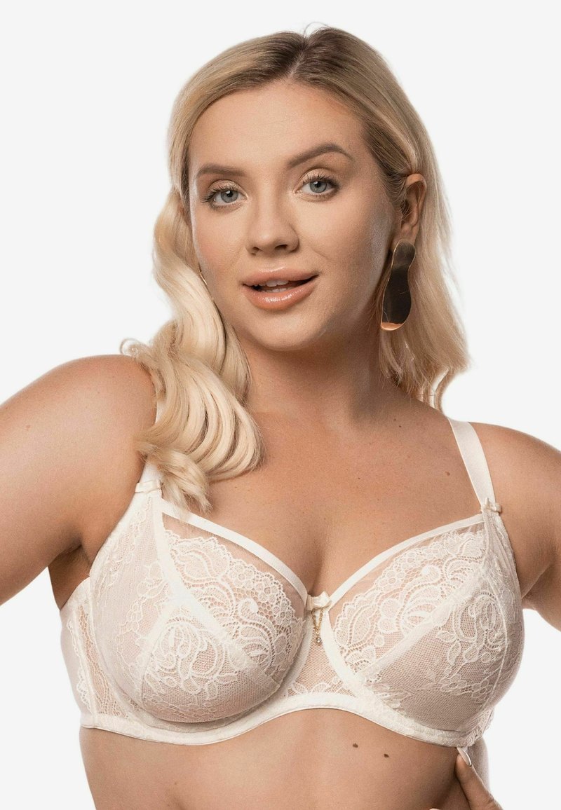Koronkowy biustonosz w kolorze kremowym z fiszbinami, przezroczystymi panelami i delikatnym detalem w postaci kokardki na środku. Regulowane ramiączka. Gładka tekstura.