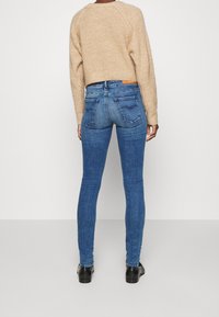 Jeans de mezclilla azul ajustados con cintura alta, que cuentan con bolsillos traseros y detalles de costura sutiles. Combinados con un suéter de punto beige.