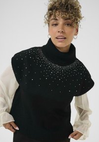 Juodas megztas turtleneck tipo džemperis su trumpomis rankovėmis, puoštas išmėtytais dirbtiniais brangakmeniais priekyje ir su raukšlėta apačia. Puikiai derinamas su balta permatoma palaidine.