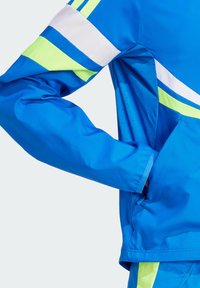 Chaqueta deportiva azul con rayas verdes y blancas, textura suave, mangas largas y un bolsillo lateral con detalles de ventilación.