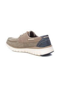 Zapatilla de lona beige con superficie texturizada, detalles en color marrón claro y un talón en azul oscuro, con una suela acolchada y ojales de cordones en dos tonos.