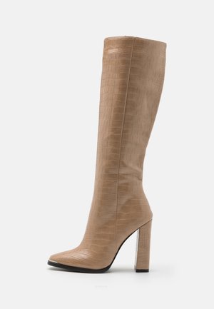 Tall beige knee-high boot with a crocodile texture, pointed toe, and block high heel against a white background.