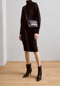 Sweater de punto negro con cuello alto, acompañado de una falda negra ajustada con cremallera lateral. Botines negros y un bolso de hombro texturizado.