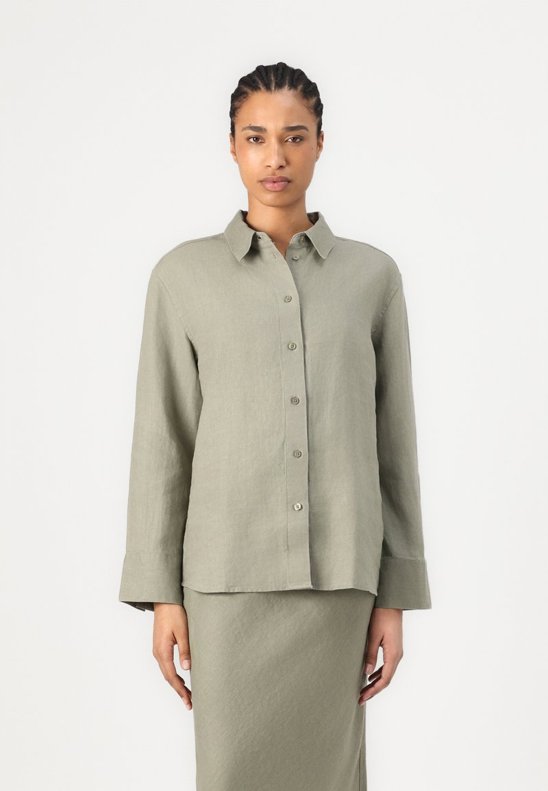 Light green button-up shirt made of textured fabric, featuring a classic collar and long sleeves, paired with a matching skirt.