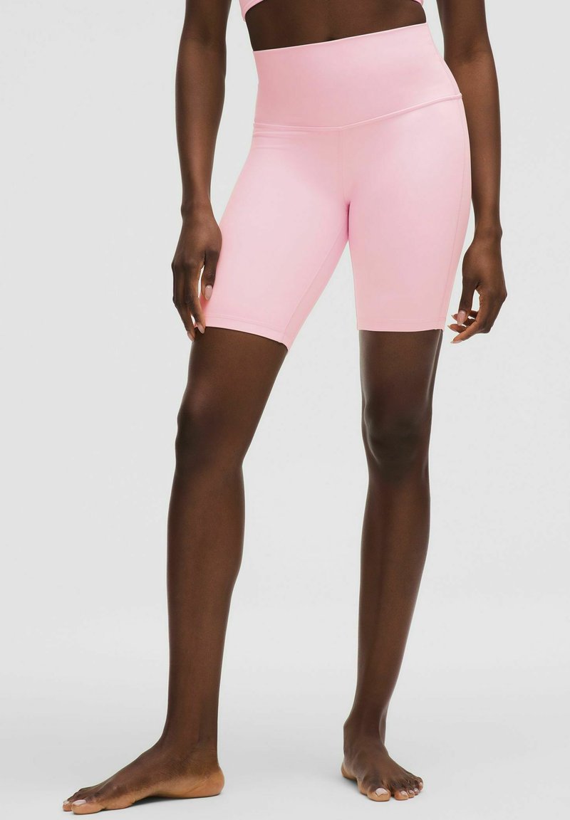 Jasnoróżowe szorty rowerowe z wysokim stanem, gładką teksturą i dopasowanym krojem, sięgające do połowy uda. Brak widocznych metalowych elementów lub wzorów.