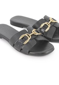 Chanclas negras de cuero liso con correas entrecruzadas y un acento decorativo de cadena dorada. Diseño de suela de perfil bajo.