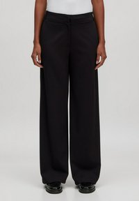 Zwarte wijde broek gemaakt van een gladde stof. Voorzien van een ritssluiting aan de voorkant, zijzakken en een hoge taille.