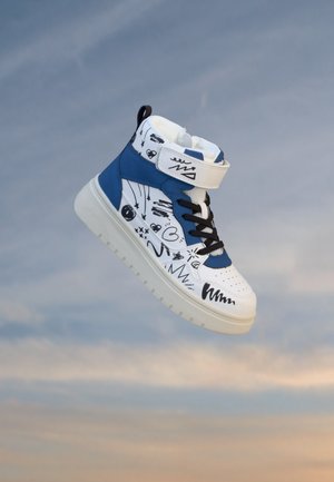 Baskets montantes blanches et bleues avec motifs griffonnés noirs, lacets noirs et une bride velcro blanche flottant sur un fond de ciel nuageux.