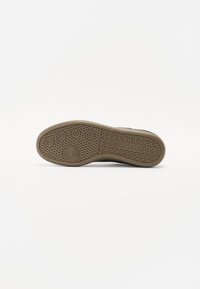 Semelle de chaussure en caoutchouc brun avec un motif texturé, présentant des designs de semelles circulaires et ovales pour l'adhérence. Forme plate avec des bords arrondis.