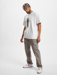 Hvid bomulds t-shirt med grafisk print af en figur og tekst. Kåret med lysegrå cargo-bukser og hvide sneakers med røde accenter.