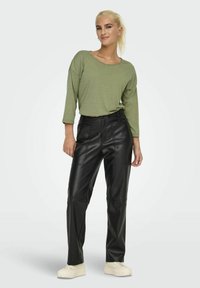 Olijfgroene gestreepte top met lange mouwen, gecombineerd met hoogstaande zwarte faux leren broek. Model draagt lichte sneakers.