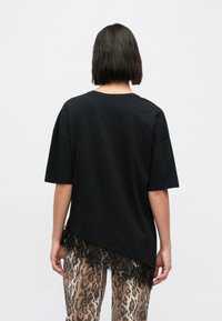 Černé tričko s krátkými rukávy a krajkovým lemem na spodním okraji, volného střihu a kulatým výstřihem, v kombinaci s kalhotami se vzorem leopardí kůže.