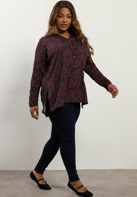 Koszula z długim rękawem, w kolorze burgundowym, z kwiatowym wzorem, z guzikami i bocznymi rozporkami, zestawiona z ciemnoniebieskimi skinny jeansami i czarnymi balerinami.