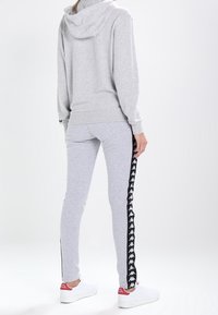 Grå bomullshuvtröja med känguruficka och dragsnöre i huvan, kombinerad med grå joggers som har svarta sidostråkar och logodetaljer. Vita sneakers.