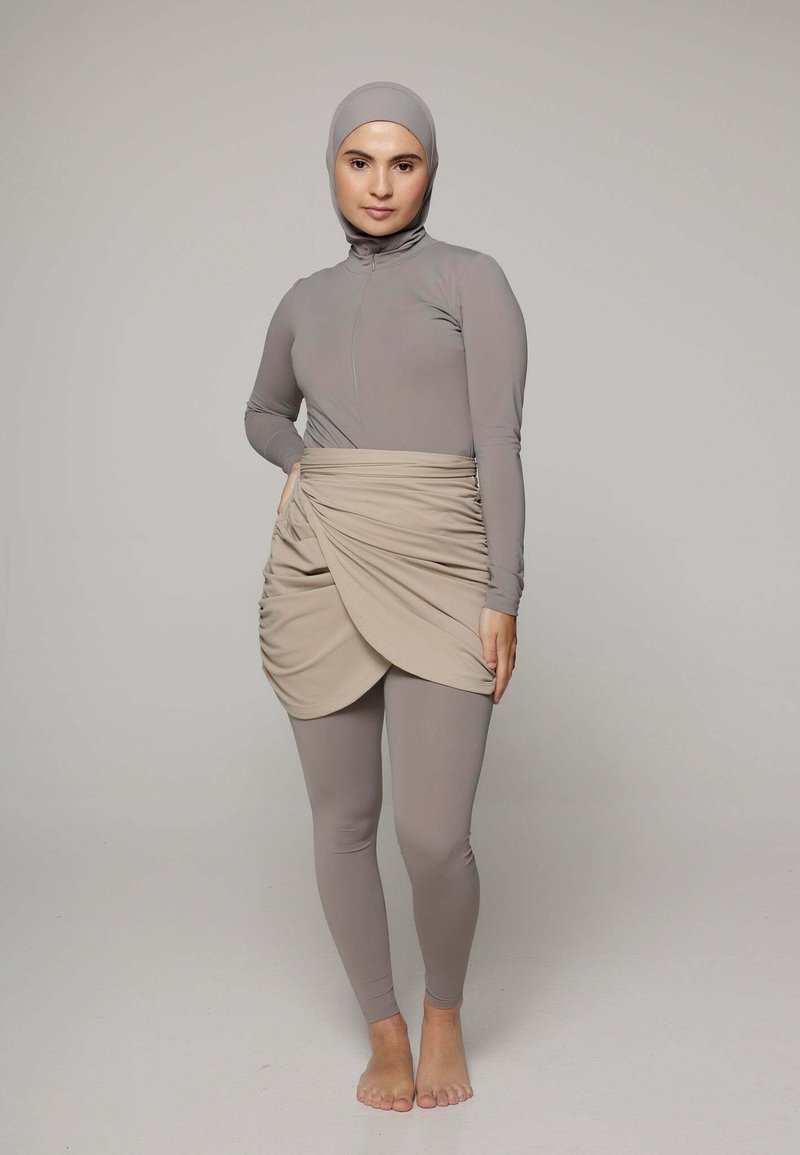 Langarm, lichtgrijs zwempak met een hoge hals. Voorzien van een beige, gedrapeerde rok overlay. Soepele, rekbare stof; getailleerd ontwerp.