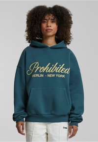 Teal hættetrøje med gyldne kursiv-tekster "Prohiberet BERLIN - NEW YORK" og en lomme fortil. Har ribbede manchetter og kant.
