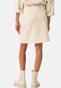 Abito cremoso, con texture in un materiale morbido, dalla linea dritta e con maniche arrotolate. Abbina stivali alla caviglia di un beige chiaro.