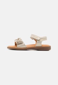 Sandales en cuir doré clair avec détail fleuri, brides ajustables et semelle en caoutchouc marron. Design ouvert pour une respirabilité et un confort optimaux.