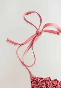 Roze stoffen tas met een bloemenpatroon aan de voorkant, met lange, gestrikte hengsels. Gladde textuur met een geknoopt strikje aan de bovenkant.