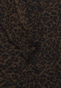 Tissu marron avec motif léopard noir et manche froncée visible avec détail de bord volanté.