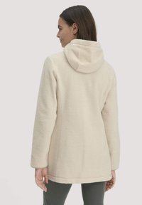 Cremefarbene Fleecejacke mit Kapuze, die eine weiche Textur, lange Ärmel und ein leicht tailliertes Design aufweist.