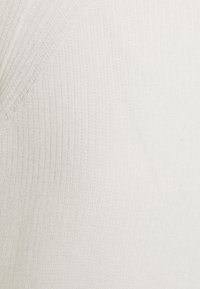 Tessuto in maglia a coste bianco con una texture sottile e design a V. Il materiale è morbido e flessibile, ideale per essere indossato a strati.