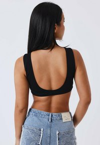 Top corto nero con scollo profondo sul retro, abbinato a pantaloni shorts in denim leggeri a vita alta di colore azzurro, con dettagli in pizzo e una toppa quadrata.