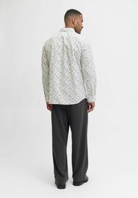 Valkoinen pitkähihaan paita kukkakuviolla, yhdistettynä tummanharmaisiin, leveisiin housuihin. Paidassa on kaareva helma ja nappikaulus.