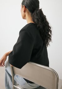 Must have pehmead lühikesed varrukad, istudes hõbedasel kokkuklapitaval toolil, kombineeritud helesiniste teksadega. Sile juuksed on ponis.