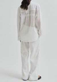 White perforated shirt and matching wide-leg pants, featuring square cutouts, relaxed fit, and textured fabric. Simple design, minimal hardware.