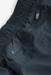 Dark blue athletic fabric featuring gathered texture, a zippered pocket, and smooth surface with stitching details throughout.