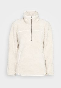 Valkoinen fleece-pulloveri, jossa on korkea kaulus, puolivetoketju ja sivutaskut. Pehmeä, teksturoitu kangas tarjoaa lämpöä.