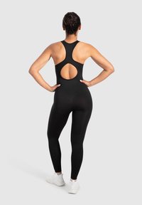 Zwarte sportieve jumpsuit met een racerback ontwerp, voorzien van een ronde uitsparing op de rug en aansluitende pijpen, gemaakt van rekbaar materiaal.