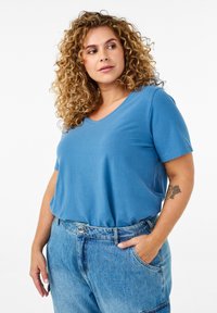 T-shirt azul de cuello en V hecho de tela suave, de manga corta, ajuste relajado, combinado con pantalones de mezclilla claros de cintura alta, con bolsillos laterales.