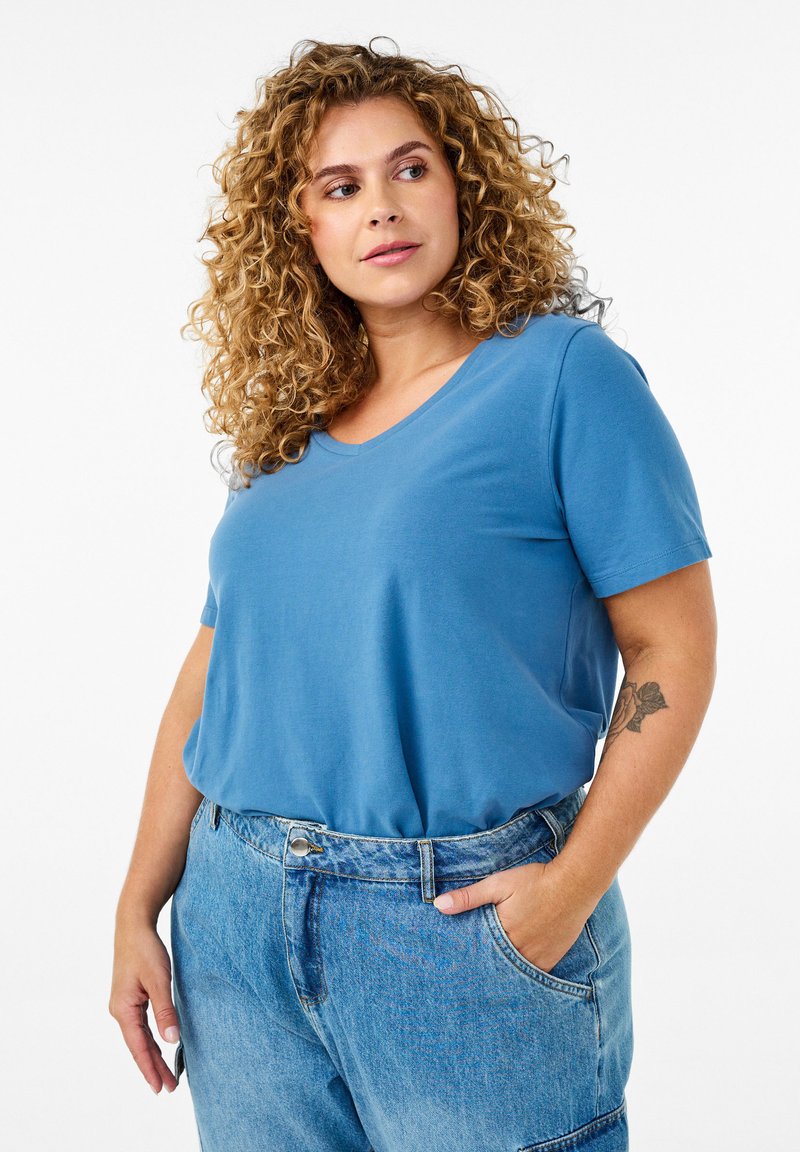 T-shirt azul de cuello en V hecho de tela suave, de manga corta, ajuste relajado, combinado con pantalones de mezclilla claros de cintura alta, con bolsillos laterales.