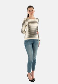 Maglione a righe a coste in crema e blu navy, abbinato a jeans azzurri. Il modello indossa tacchi a punta neri. Design semplice e aderente.