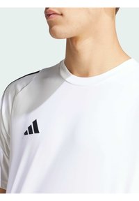 T-shirt de sport blanc avec un col rond, présentant un logo Adidas noir et des accents noirs sur les épaules. Texture lisse.