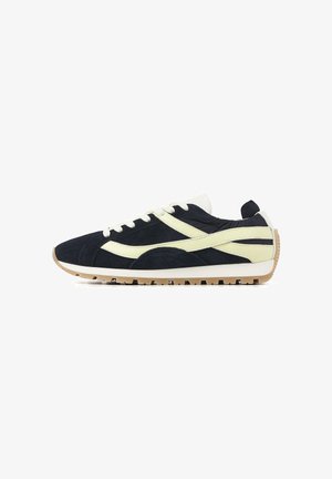 Schwarzer und beiger Freizeitschuh mit weißen Schnürsenkeln, beigen Seitenstreifen und einer geriffelten hellbraunen Gummisohle.