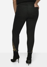 Los jeans skinny de mezclilla negra presentan un patrón floral dorado en los puños, dobladillo deshilachado y un diseño tradicional de cinco bolsillos.