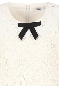 Blusa bianca in pizzo con motivo floreale, scollo rotondo con un fiocco in raso nero e una zip nascosta sul retro.