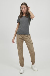 Grå kortærmet t-shirt parret med khaki cargo-bukser med elastiske manchetter og sidelommer. Modellen har hvide sneakers på.