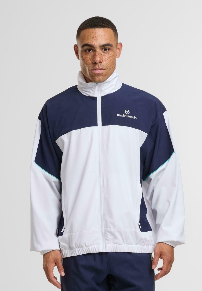 Tengerészkék és fehér színblokkokkal ellátott szélálló dzseki, magas gallérral, cipzáras záródással, rugalmas mandzsettákkal és mellkason lévő márkajelzéssel. Simogató, könnyű anyag.