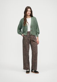 Grønn strikket cardigan med tre knapper, parret med brune bukser med leopardmønster i vid modell. Modellen har på seg svarte sneakers med hvite detaljer.