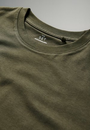 Oliivroheline puuvillane ümar kaelusega t-särk sujuva tekstuuriga. Sellel on õmmeldud servad ja silt, millel on kirjas "THE SET" koos "MADE IN BANGLADESH".