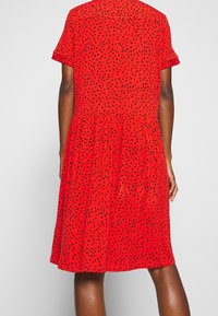 Červené šaty s krátkým rukávem, černým tečkovaným vzorem, volným střihem, s volánkovou sukní, texturovaným materiálem a kulatým výstřihem.