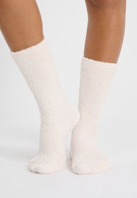 Calcetines de crema esponjosos hechos de un material suave, con textura acanalada, diseño hasta la rodilla y una apariencia acogedora.