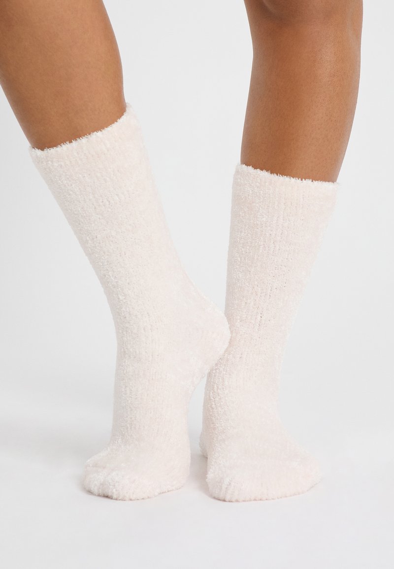 Calcetines de crema esponjosos hechos de un material suave, con textura acanalada, diseño hasta la rodilla y una apariencia acogedora.